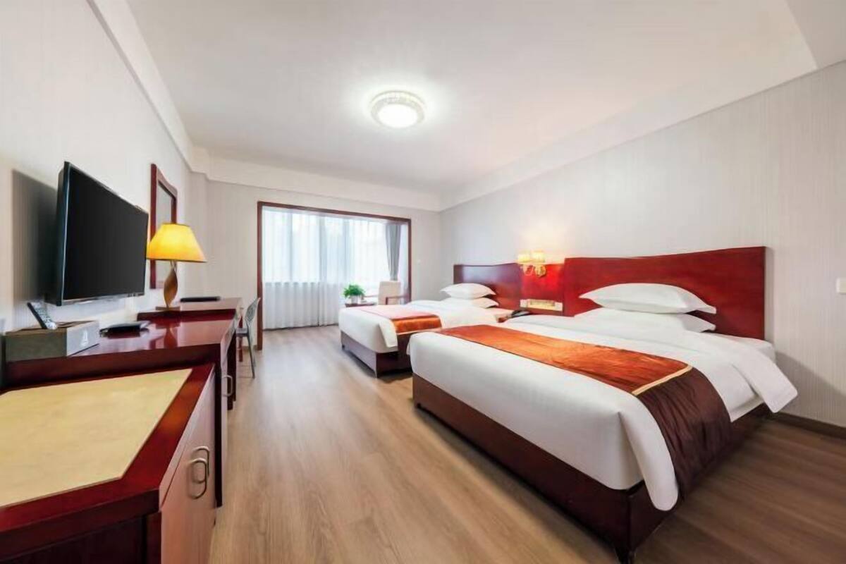 Una habitación de hotel con cama, escritorio, televisor y ventana.