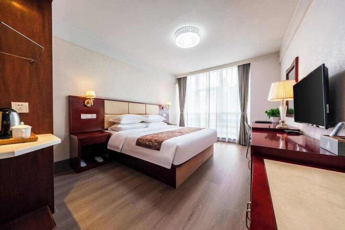 Habitación de hotel con cama, escritorio, televisión y ventana con cortinas.