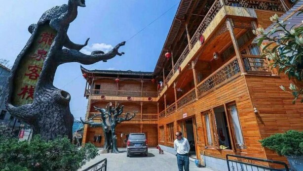 A traditional wooden building with a balcony and a large tree sculpture in front. - Zhang Jiajie Longquan Inn (Zhangjiajie)