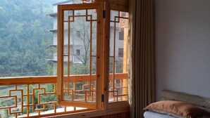 A room with a bed, a window with a wooden lattice design, and a view of a mountainous landscape. - Zhang Jiajie Longquan Inn (Zhangjiajie)