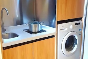 Une cuisine équipée d’un évier en acier inoxydable, d’une casserole posée sur le plan de travail et d’un lave-linge à chargement frontal.