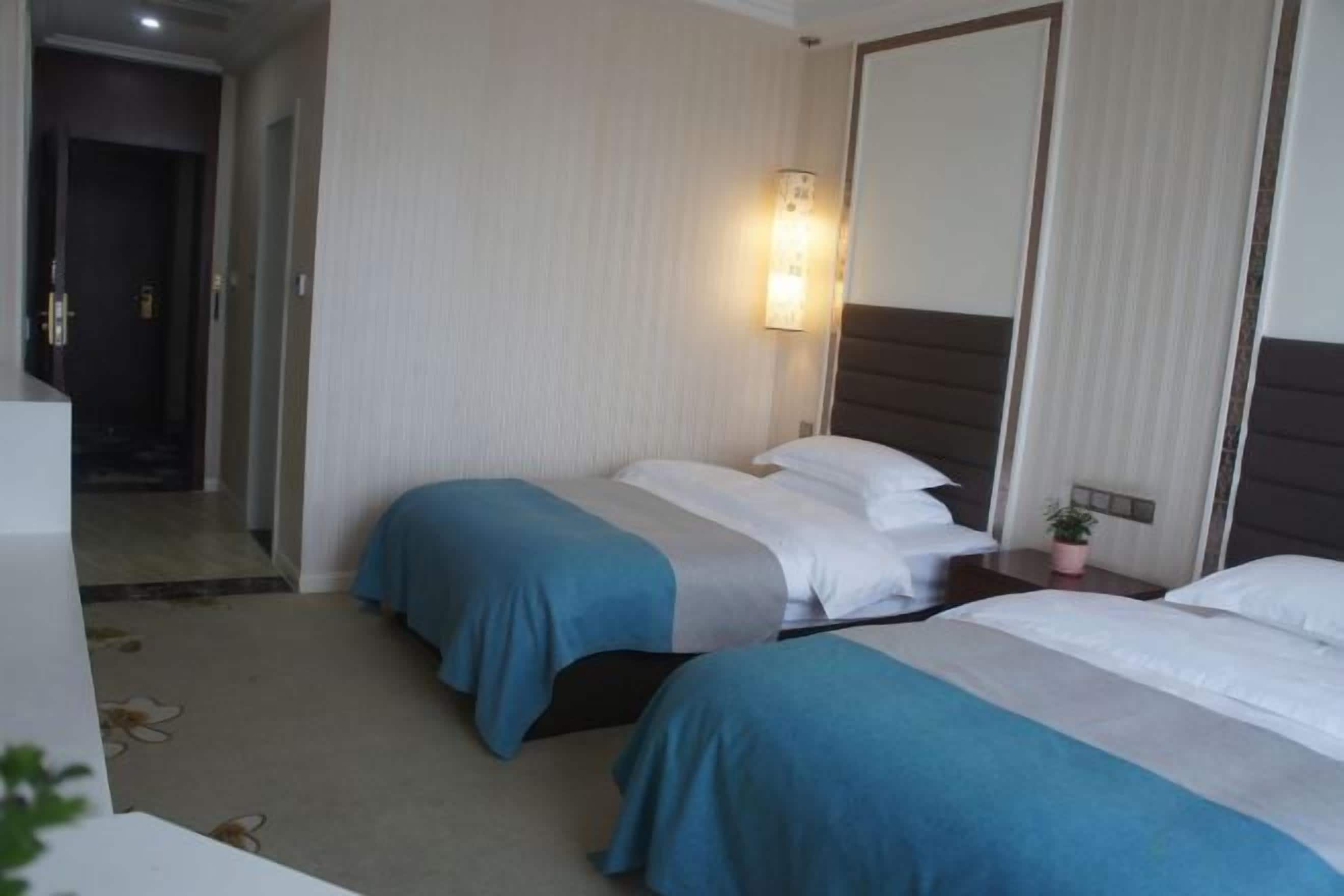 Habitación de hotel con dos camas, una mesita de noche con lámpara y un espejo.