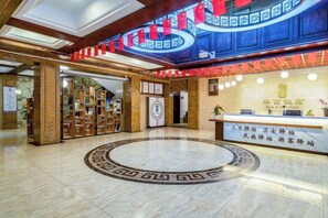A lobby with a reception desk, a circular patterned floor, and a large blue wall with red accents. - Huaxi Hotel Dujiangyan (Chengdu)