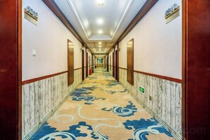 Un pasillo de hotel con suelo de mármol, puertas de madera y una zona alfombrada.