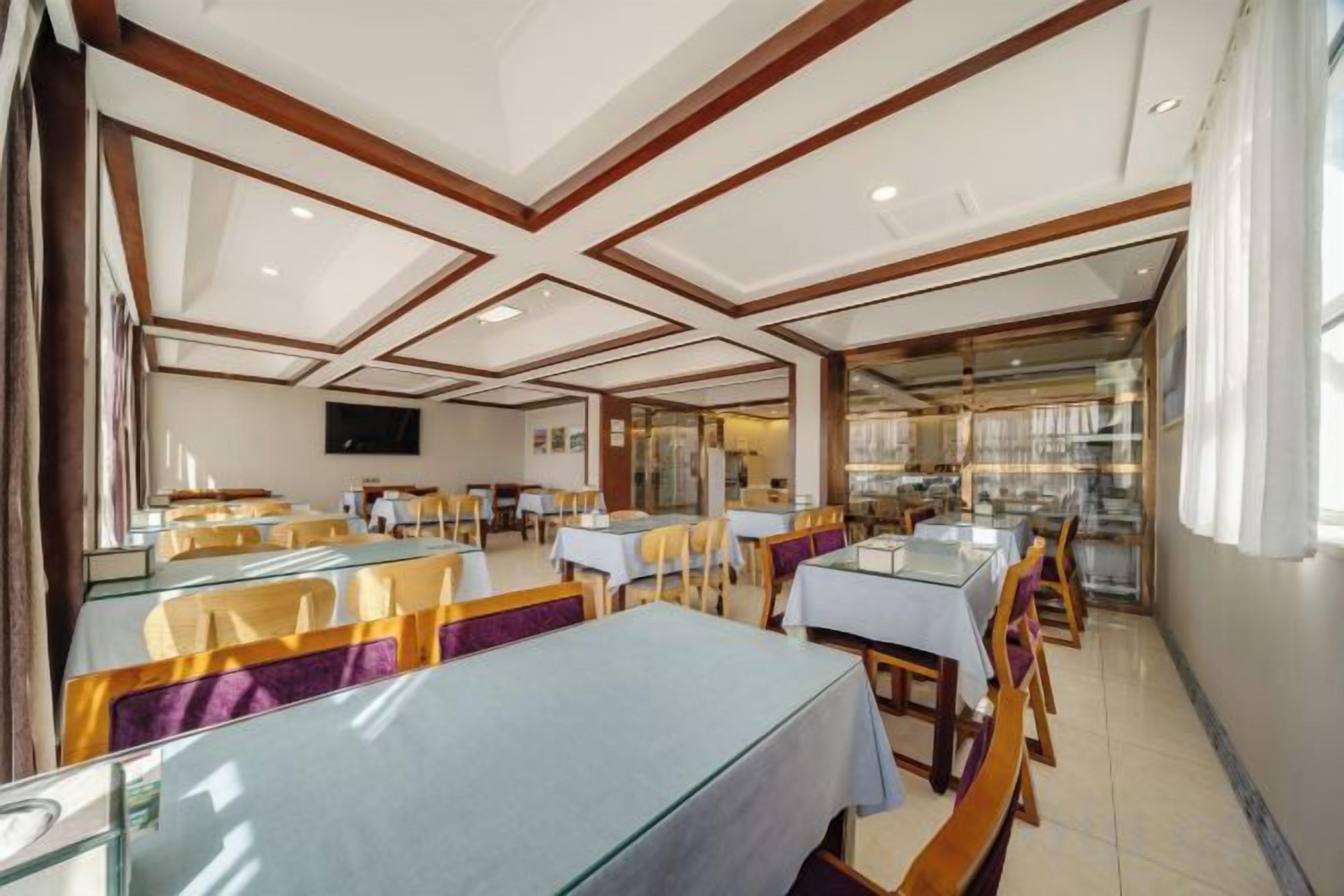 Un restaurante con varias mesas y sillas, un televisor en la pared y vistas al exterior.