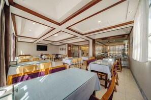 A restaurant with multiple tables and chairs, a television mounted on the wall, and a view of the outdoors. - Huaxi Hotel Dujiangyan (Chengdu)