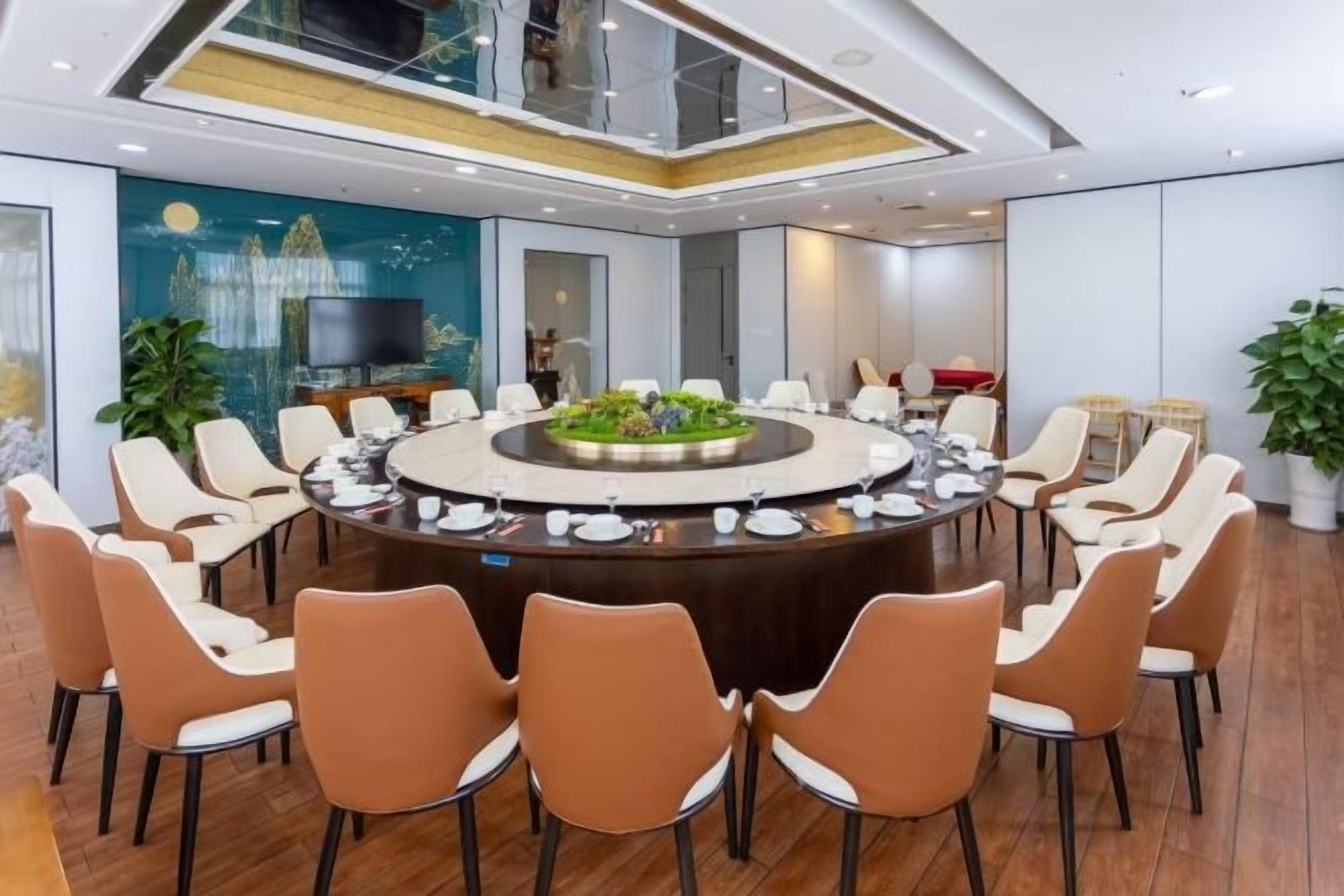 A conference room with a round table surrounded by chairs, a television, and a large window.