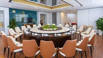 A conference room with a round table surrounded by chairs, a television, and a large window.