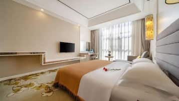 A hotel room with a large bed, a flat-screen TV mounted on the wall, a bedside table, and a window with curtains.