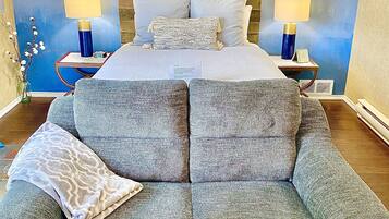 A bedroom with a large bed, two bedside tables with lamps, a grey sofa, and a decorative wall.