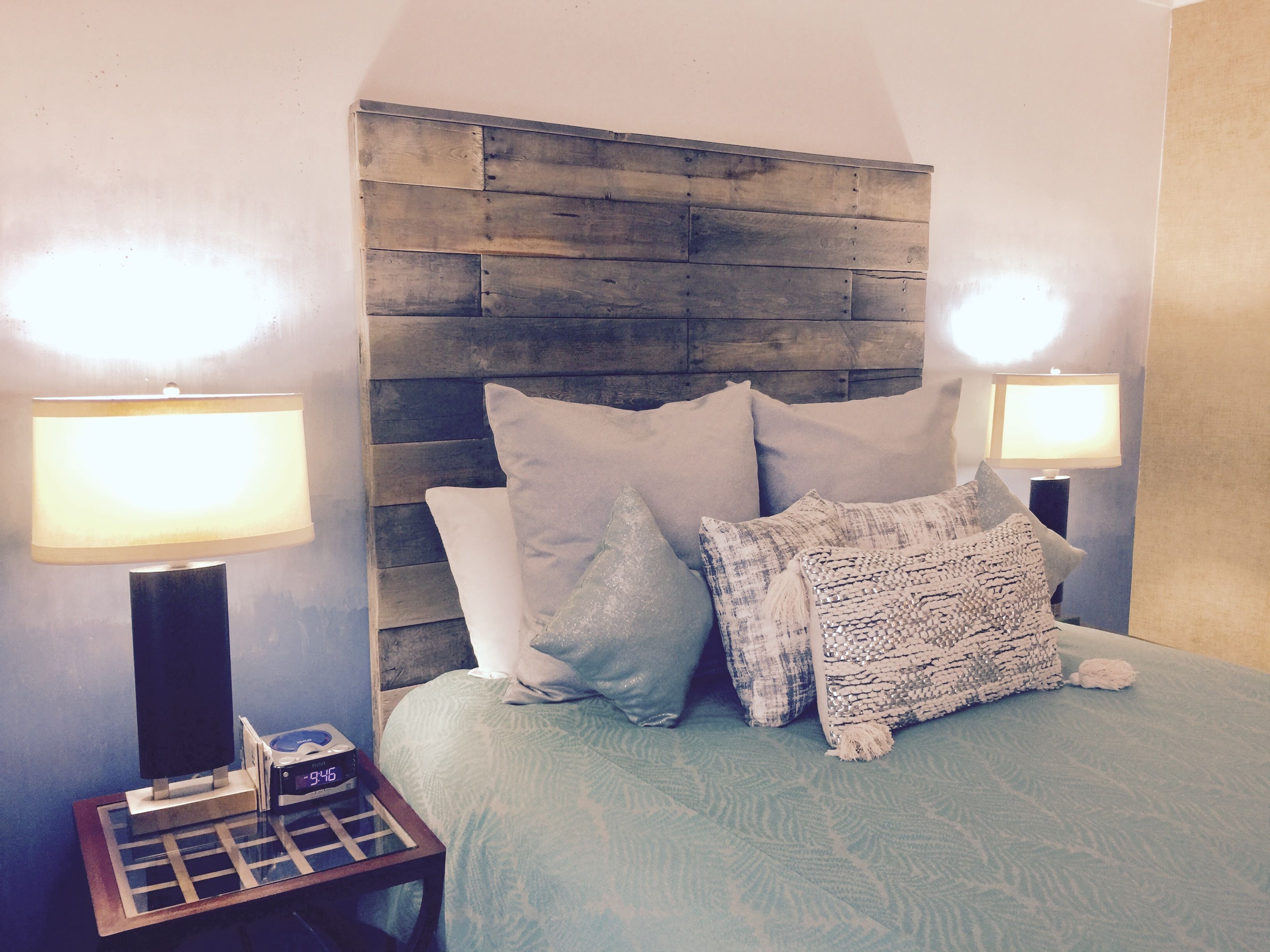 A bedroom with a wooden headboard, a bed with a light blue bedspread, and two bedside lamps.