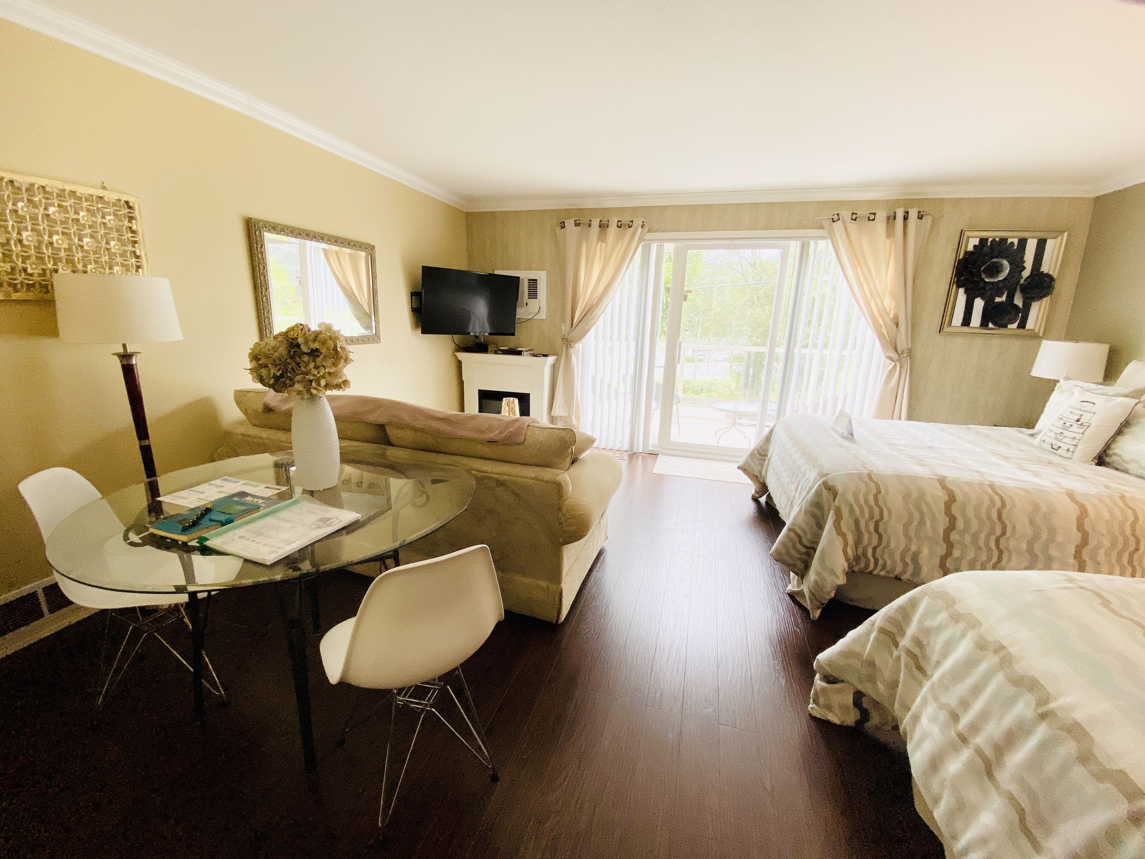 Habitación de hotel con una mesa de vidrio, un sofá, una cama con ropa de cama estampada, un televisor y una chimenea.