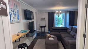 Uma sala de estar moderna com sofá, puf e TV fixada na parede.