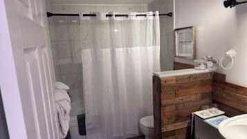 Un baño con cortina de ducha, inodoro, lavabo y tocador de madera.