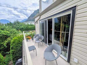 A balcony with two chairs and a table, overlooking a lush garden and mountains.