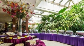 A banquet hall with round tables covered in purple tablecloths, a large floral centerpiece, and lush indoor plants. - The Twenty First Century Hotel - Beijing (Beijing)