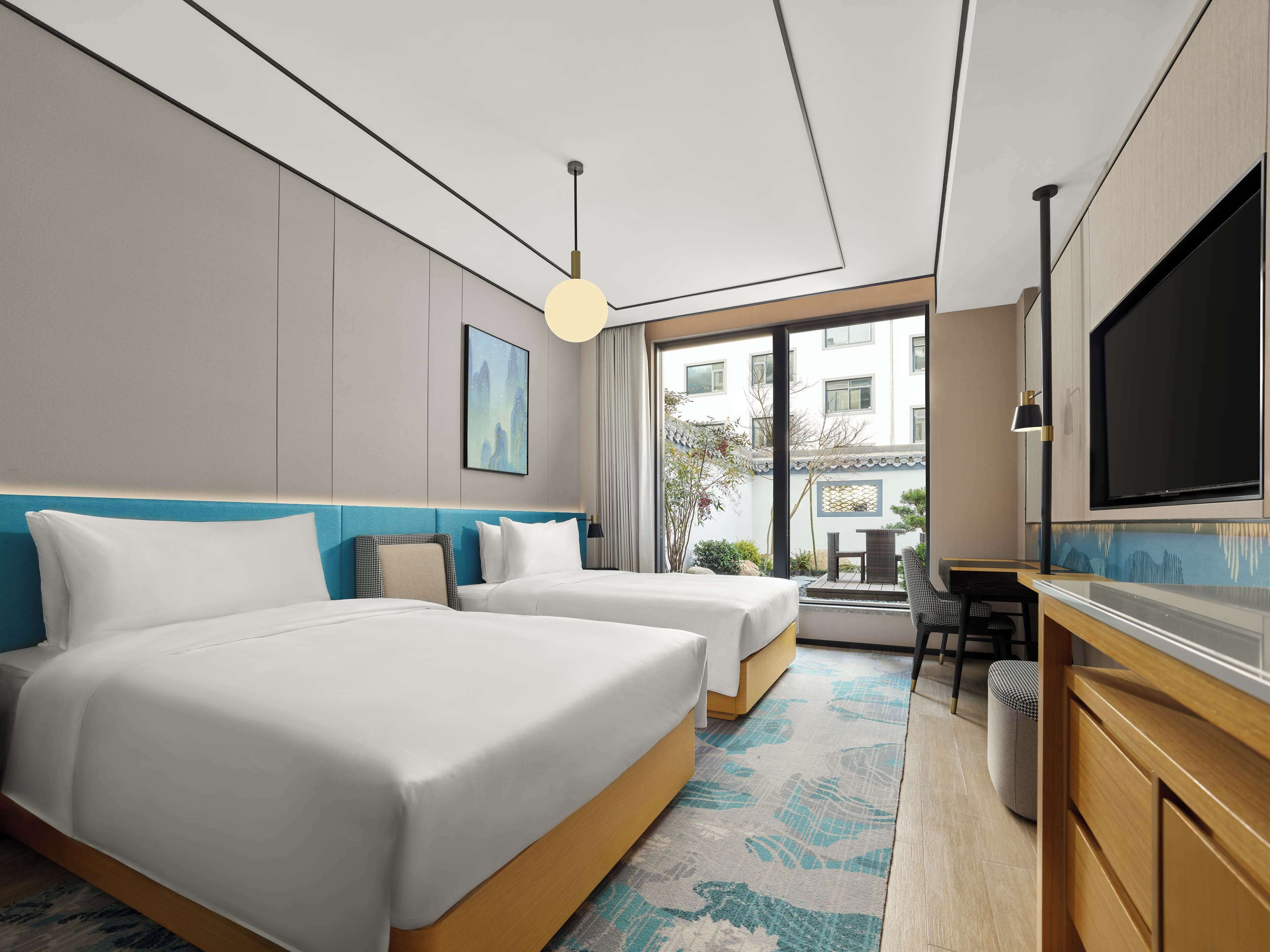 Habitación de hotel con dos camas, televisión, escritorio y vistas al exterior.