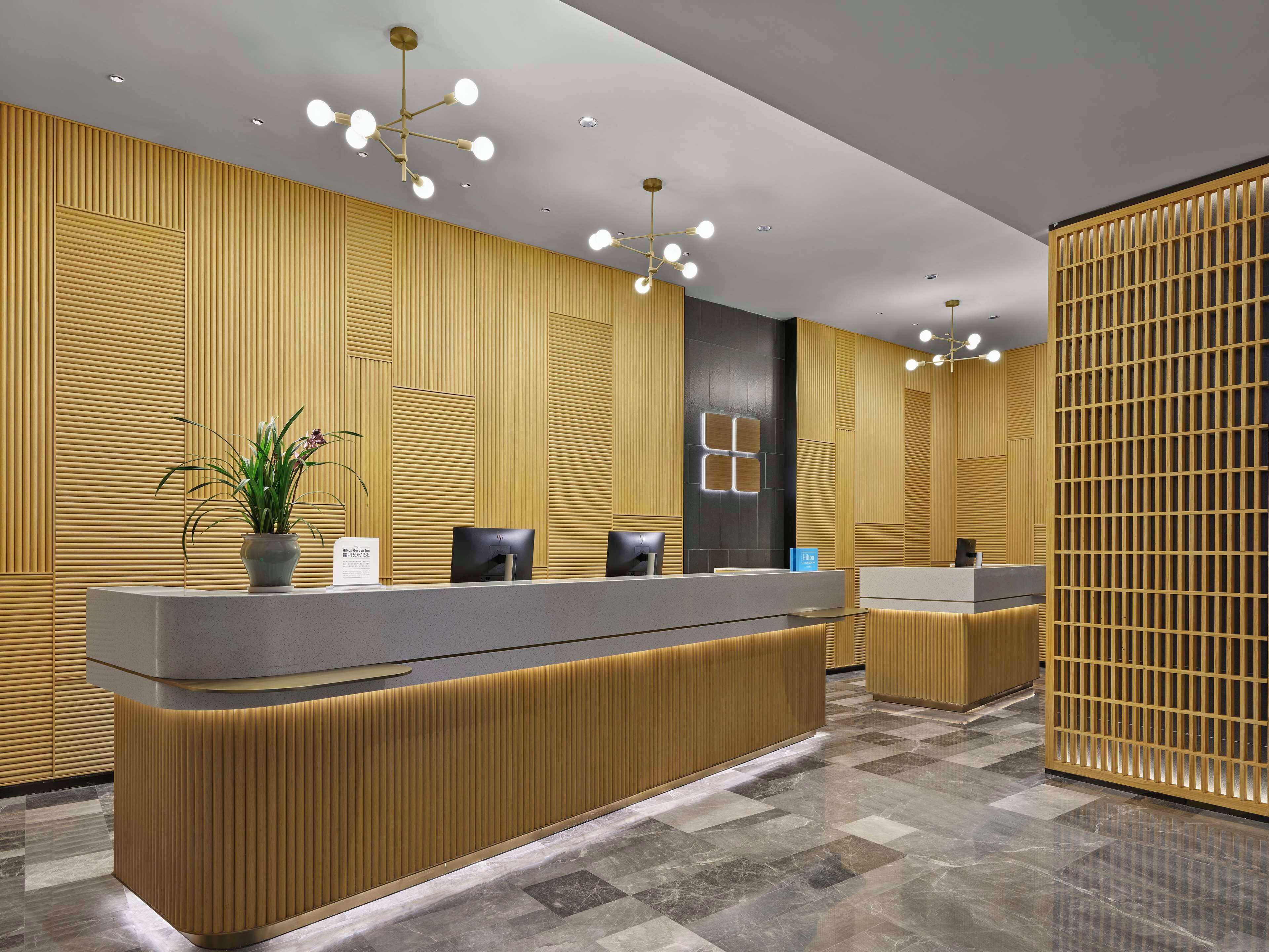 A modern reception area with a wooden panel wall, a reception desk, and a potted plant.