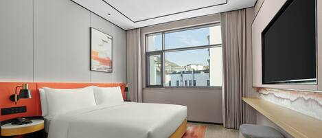 A modern hotel room with a bed, a desk, a TV, and a window with a view of buildings.