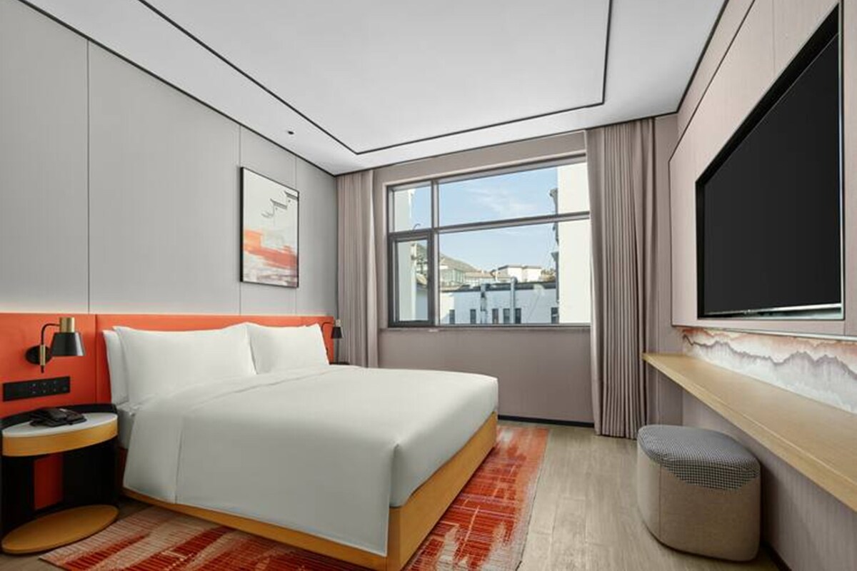 Una habitación de hotel con cama, mesita de noche, televisor y ventana con vistas.
