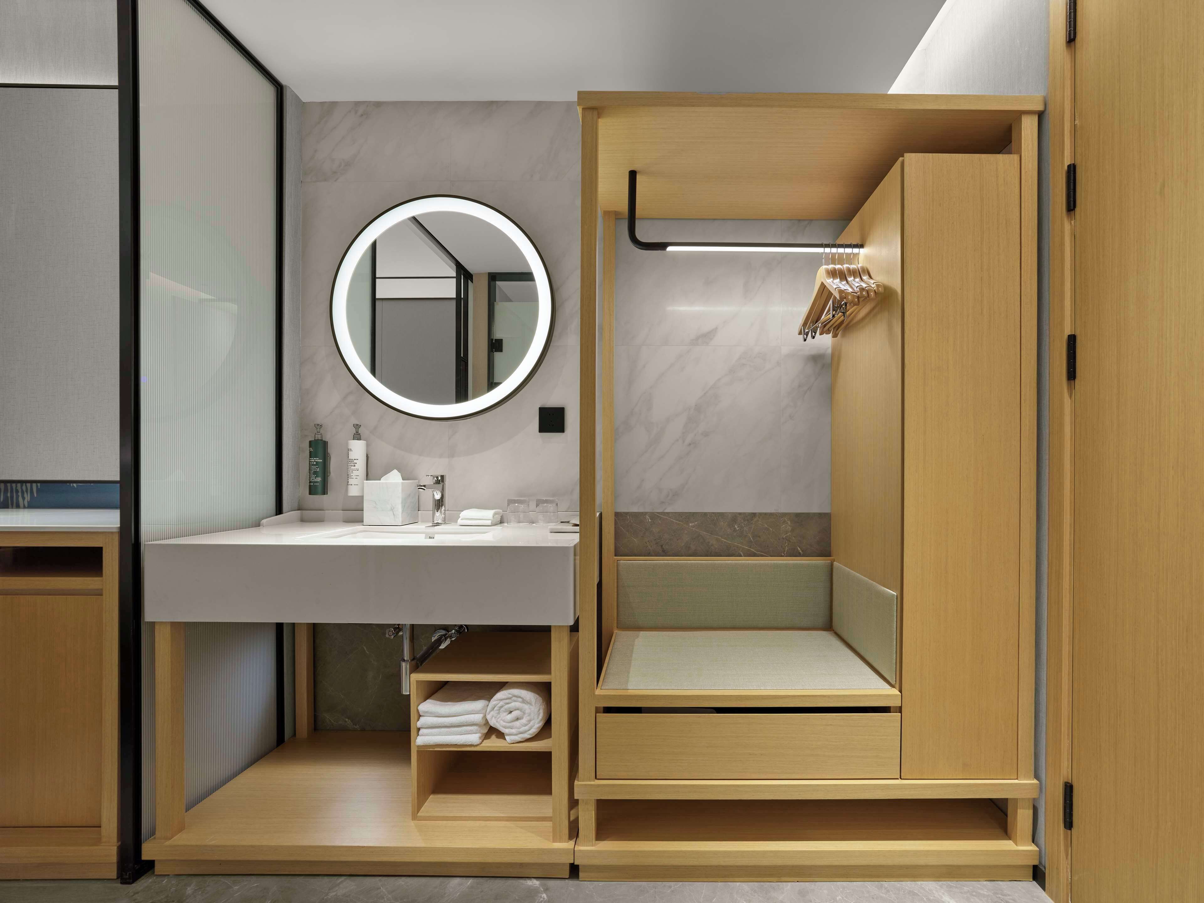 A compact, modern bathroom with a built-in vanity, a round mirror, and a shower area.