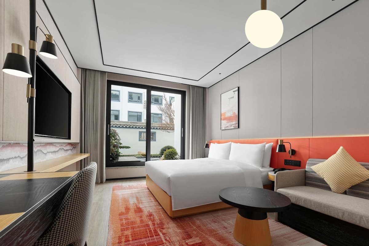 Ένα σύγχρονο δωμάτιο ξενοδοχείου με κρεβάτι, καναπέ, γραφείο και ένα μεγάλο παράθυρο.