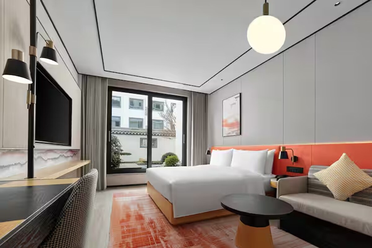 Habitación de hotel moderna con cama, sofá, televisor y vistas al exterior.