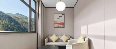 A modern room with a large window, a round table, a sofa with cushions, and a hanging light fixture.