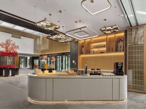 Un moderno vestíbulo de hotel con un mostrador de recepción central, iluminación decorativa y una planta grande.