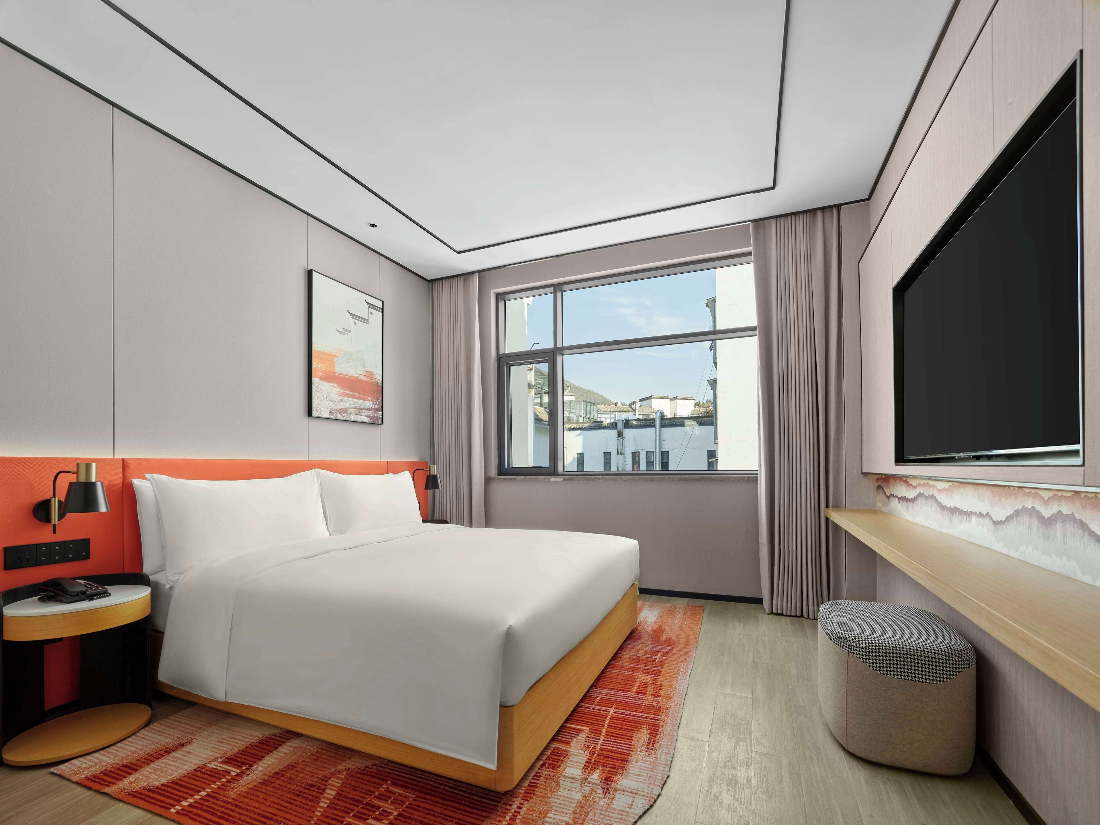 Een moderne hotelkamer met een groot bed, een bureau, een televisie en een raam met uitzicht op gebouwen.
