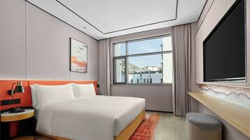 Habitación de hotel moderna con una cama grande, un escritorio, un televisor y una ventana con vistas a edificios.