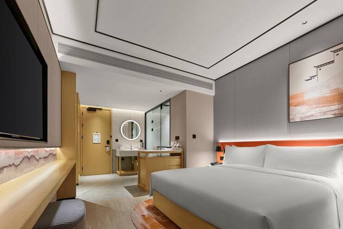 Habitación de hotel con una cama grande, televisor, baño con espejo y un cuadro en la pared.