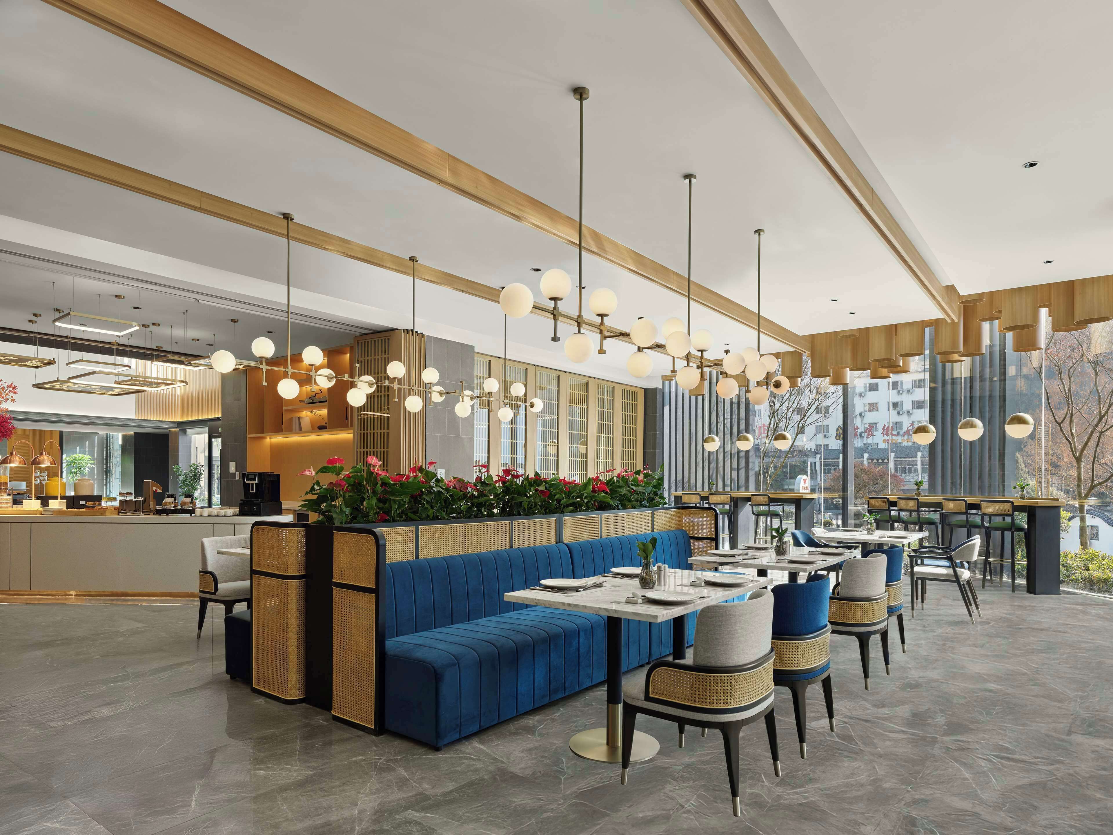 Interior moderno de restaurante con sofá azul, mesas de comedor y lámparas esféricas colgantes.