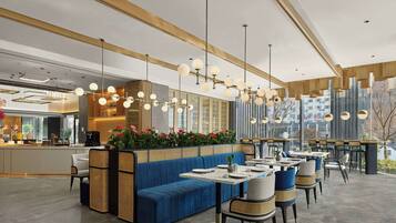 Interior moderno de restaurante con sofá azul, mesas de comedor y lámparas esféricas colgantes.