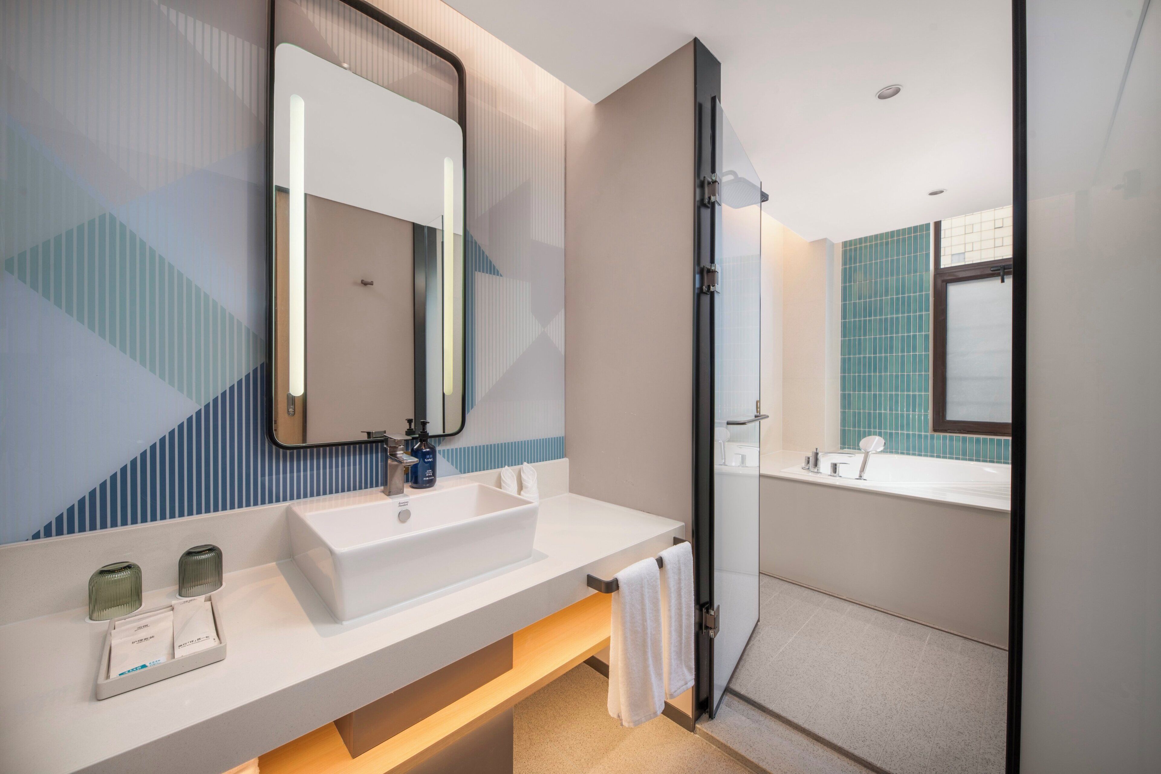A modern bathroom with a large mirror, a white sink, and a glass shower enclosure.
