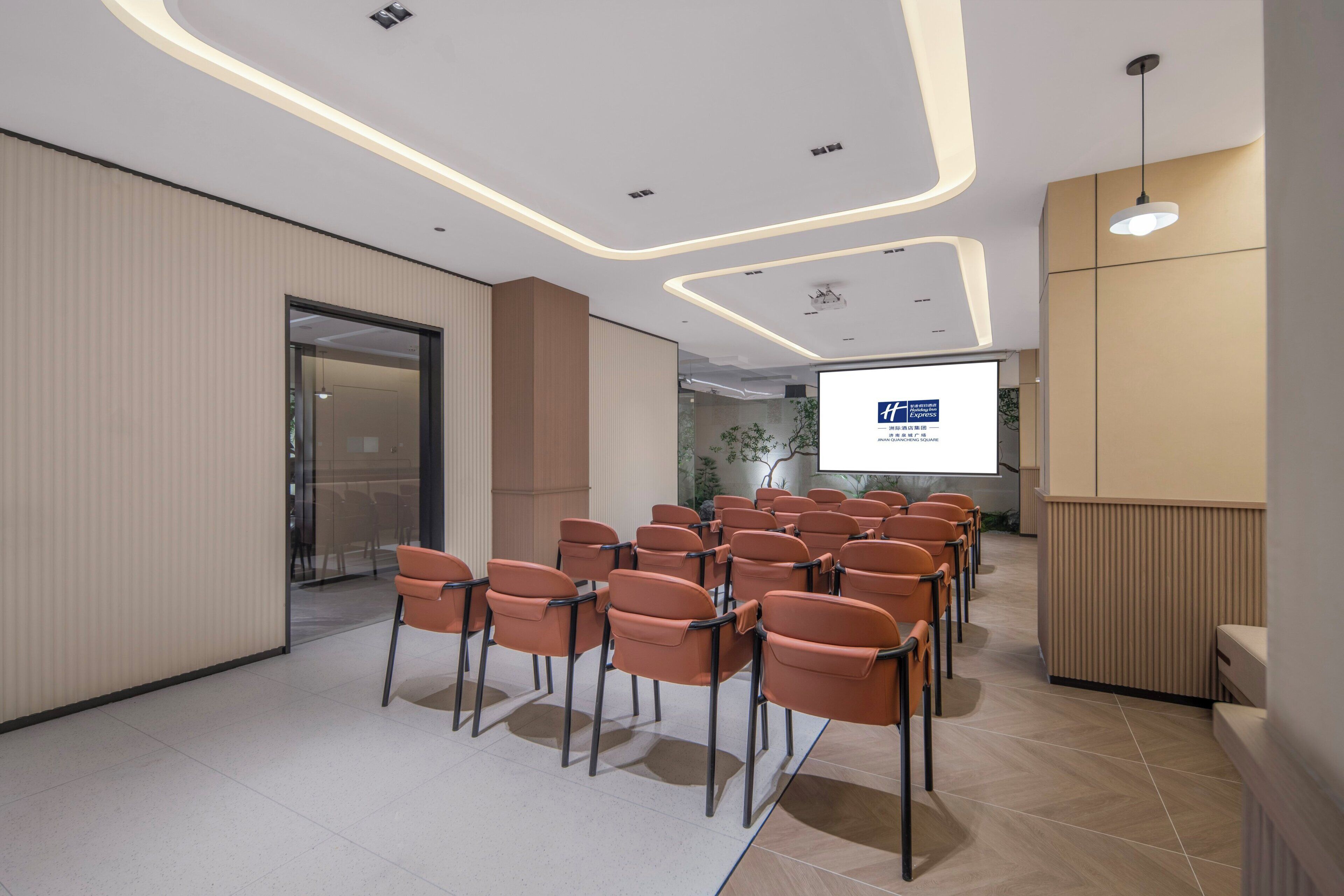 A conference room with rows of chairs, a projection screen, and a reception desk.
