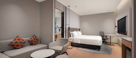 Una habitación de hotel moderna con un sofá, una mesita redonda, una cama, un escritorio y un televisor.