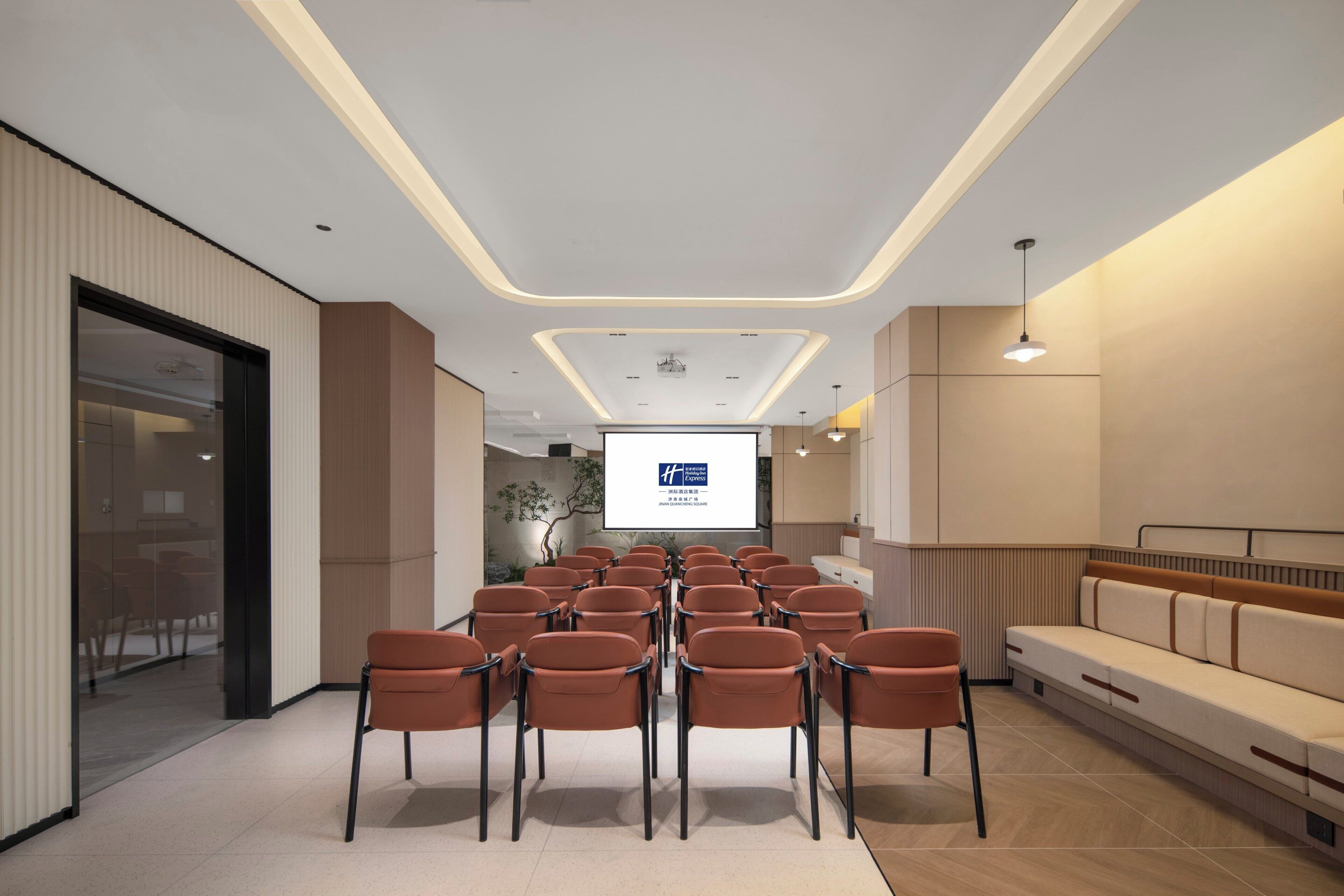 Une salle de conférence avec des rangées de chaises, un écran de projection et un canapé.