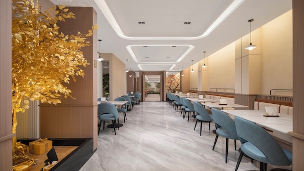 Un moderno vestíbulo de hotel con un mostrador de recepción alargado, sillas azules y un árbol dorado decorativo.