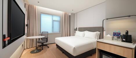 A hotel room with a bed, a desk, a chair, a television, a minibar, and a window with curtains.