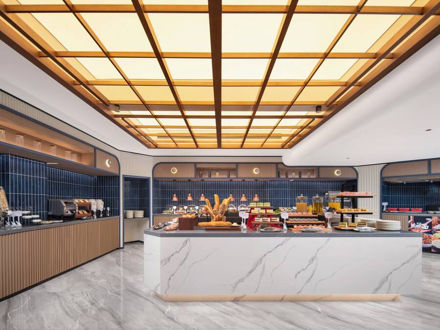 Un moderno vestíbulo de hotel con un mostrador de recepción de mármol central, un techo alto con un diseño de cuadrícula y una pared con azulejos azules.