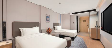 Habitación de hotel con dos camas, una mesita, un sofá, un televisor y la puerta del baño.