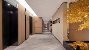 Un pasillo moderno de hotel con ascensores, una recepción y una decorativa escultura de árbol dorado.