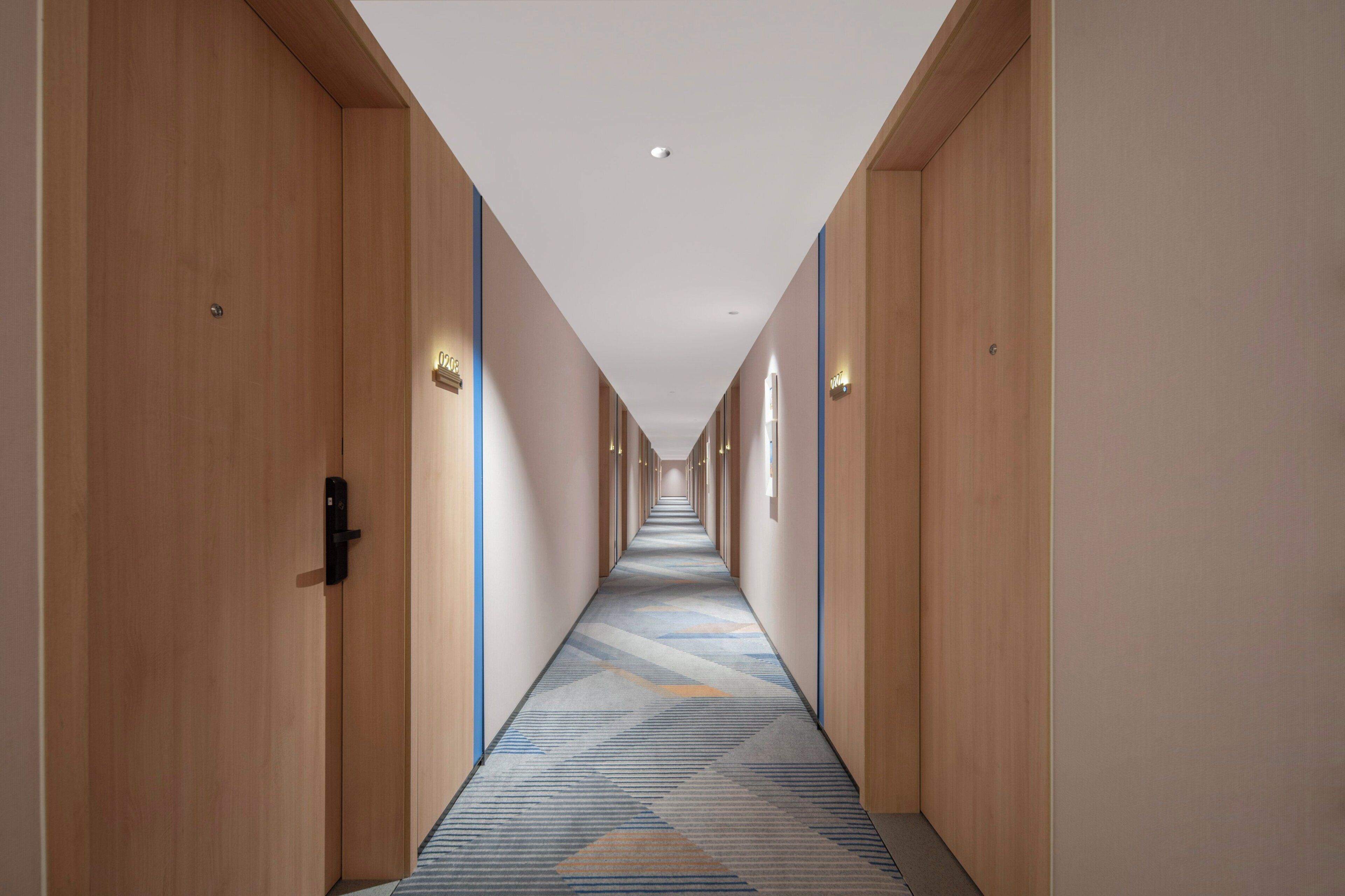 Ein langer, schmaler Hotelkorridor mit Holztüren auf beiden Seiten und einem gemusterten Teppich.