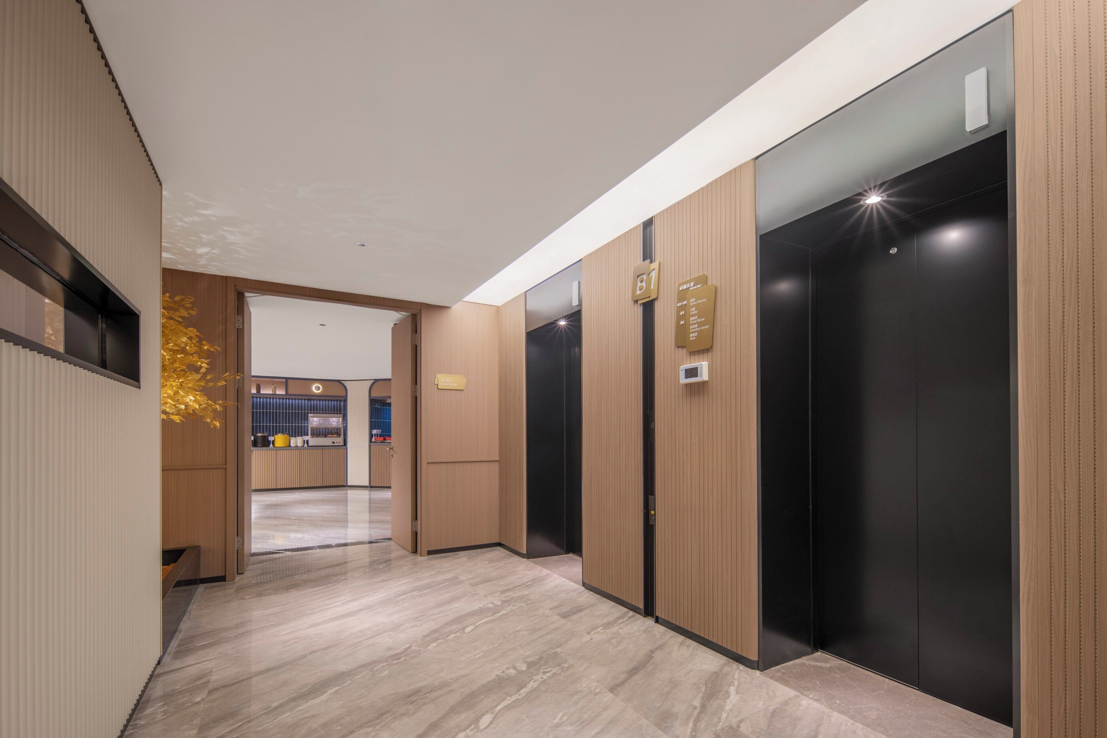 A modern hotel corridor with wooden paneling, marble flooring, and black elevators.