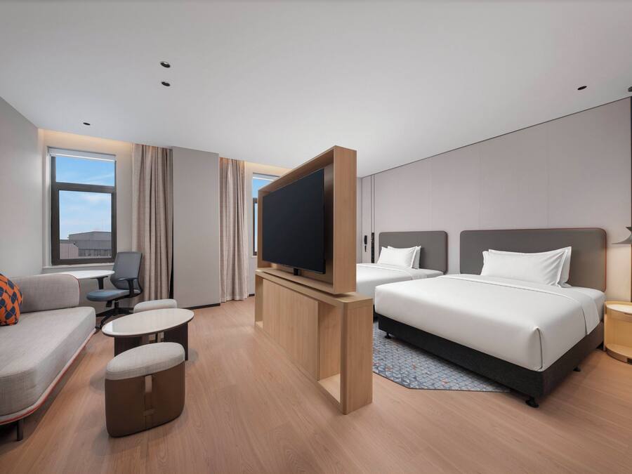 A hotel room with a sofa, two beds, a TV, a desk, and a window.