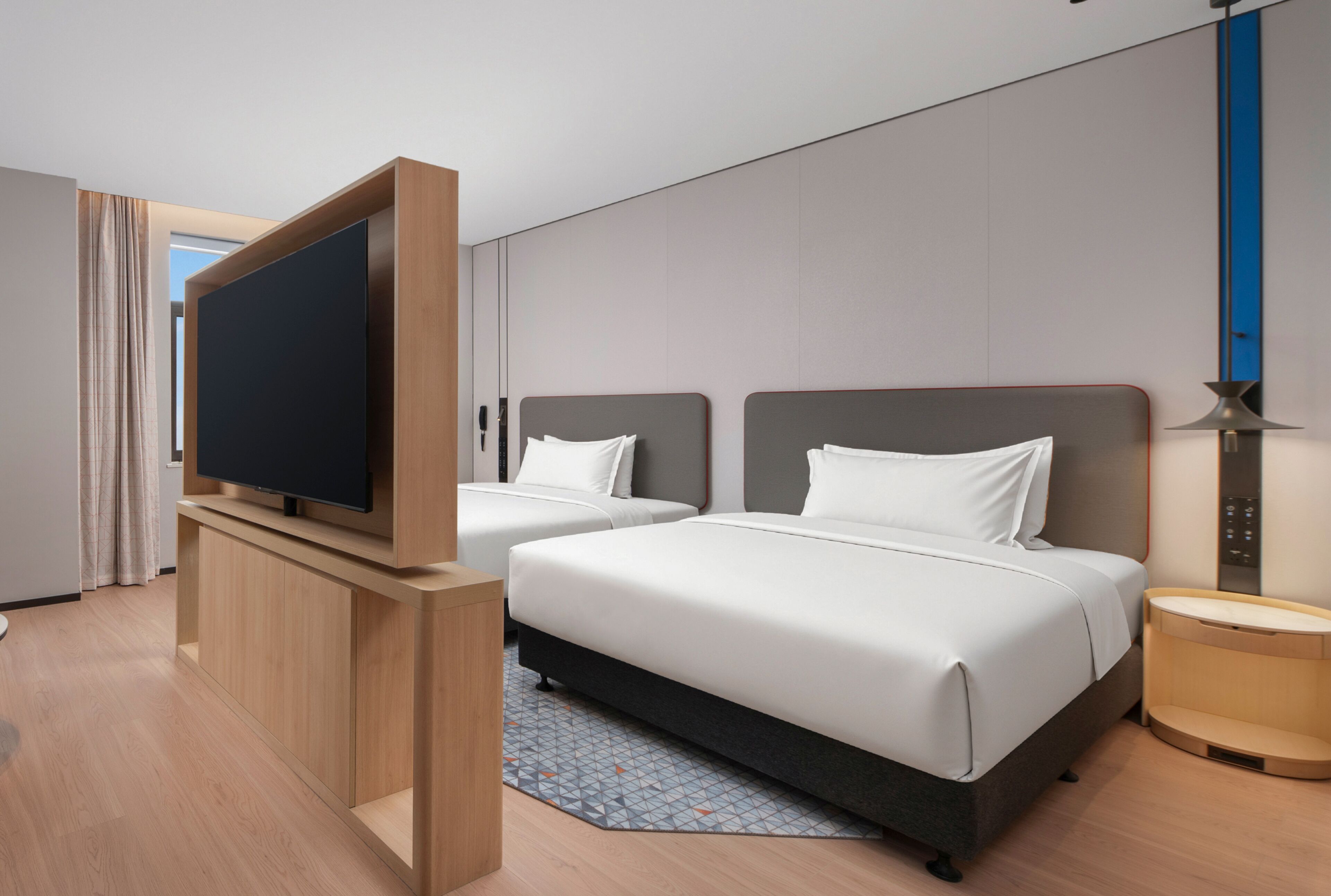 A hotel room with two beds, a TV, a desk, and a lamp.