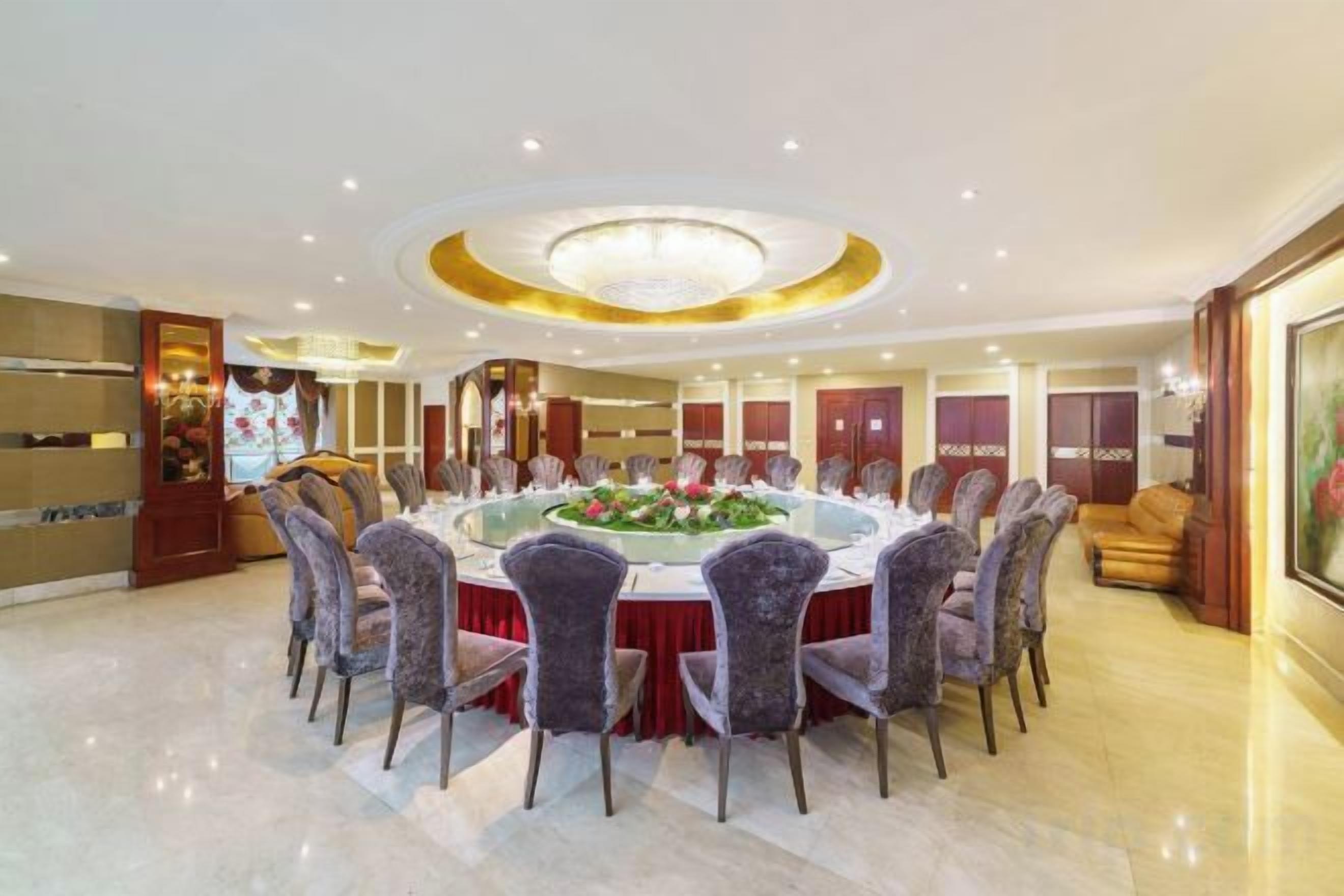 A spacious dining area with a round table surrounded by chairs, a chandelier, and a decorative centerpiece.