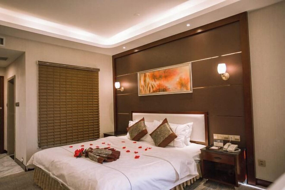 A hotel room with a large bed, a bedside table with a phone, and a painting on the wall.