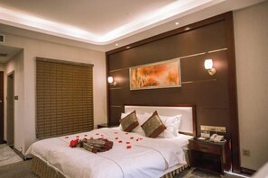 A hotel room with a large bed, a bedside table with a phone, and a painting on the wall. - Korla Pear City Garden Hotel (Korla)